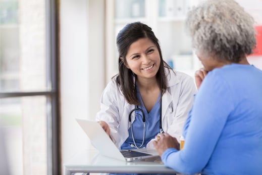 Young doctor uses laptop while sitting with senior patient